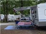 A trailer in a site with a bench and chairs at FORT WILDERNESS CAMPGROUND AND RV PARK - thumbnail