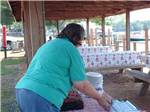 Woman in green shirt setting out hot dogs on tables at MOON LANDING RV PARK & MARINA - thumbnail