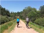 A couple riding bikes on a dirt road at Custer's Gulch RV Park & Campground - thumbnail