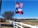 A USA and Texas flag hanging by a white fence at CANTON I-20 RV PARK - thumbnail