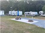 An empty gravel site with a table and fire pit at FOUR OAKS LODGING & RV RESORT - thumbnail