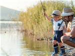 View larger image of A man fishes with a little boy in a lake at MADISON VINES RV RESORT  COTTAGES image #10