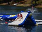 View larger image of Kids on an inflatable slide in the lake at DAVIS LAKES RV PARK AND CAMPGROUND image #5
