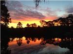 Orange and red sunset over lake with reflective trees at BONITA LAKE RV RESORT - thumbnail