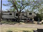View larger image of A fifth wheel trailer under a tree with a picnic table at OVERNITE RV PARK image #12