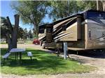 A motorhome in a gravel pull thru RV site at VILLAGE OF TREES RV RESORT - thumbnail