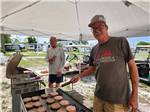 Two men barbecuing hamburgers and hot dogs at CYPRESS CAMPGROUND & RV PARK - thumbnail