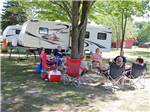 People gathered under a tree by their RV site at HOUGHTON LAKE TRAVEL PARK CAMPGROUND - thumbnail