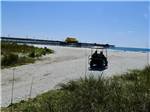 A couple driving a golf cart to the beach at APACHE FAMILY CAMPGROUND & PIER - thumbnail