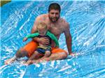 A dad and son going down a slip and slide at COUNTRY ROADS CAMPGROUND - thumbnail
