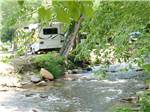 A trailer backed in by a running river at HAPPY HOLIDAY CAMPGROUND - thumbnail