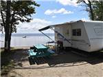 A travel trailer at an RV site next to the water at GLENROCK COTTAGES & TRAILER PARK - thumbnail