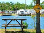 View larger image of A picnic table by the water at SUNDANCE LAKES RV RESORT image #7