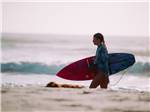 Surfer walks with board along the beach at CIRCLE CREEK RV RESORT - thumbnail
