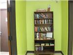 View larger image of A bookcase laden with books against a green wall at ELK CREEK RV PARK image #3