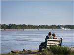 View larger image of A couple sitting on a bench looking at water at TOM SAWYERS RV PARK image #2