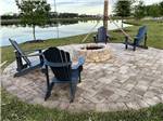 Circular brick fire pit area with black adirondack chairs at ST AUGUSTINE RV RESORT - thumbnail