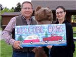 A couple holding up a Welcome Home sign at YELLOWSTONE'S EDGE RV PARK - thumbnail
