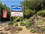 View larger image of Park sign at entrance with small waterfall feature at SMOKY BEAR CAMPGROUND AND RV PARK image #1