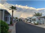 View larger image of A campground road lined with park models with rainbow in background at SUNRISE RV RESORT image #5