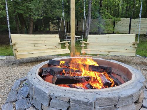 Two bench swings next to a burning fire pit at FIELD & STREAM RV PARK