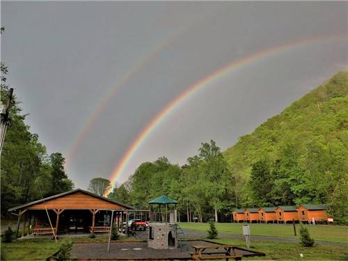 Double rainbow in background of wooden cabin and playground at PIGEON RIVER CAMPGROUND