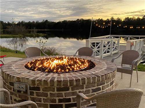 A brick fire pit blazes with serene lake in the background at CREEKFIRE RESORT