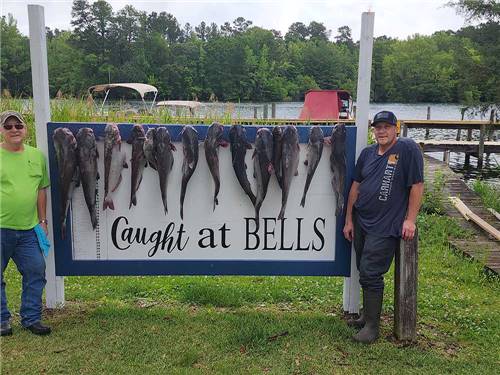 Two men standing by a sign with the fish they caught at BELLS MARINA RV RESORT