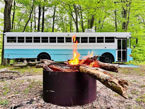 A burning fire pit with a bus in the background at DANCING FIRE GLAMPING AND RV RESORT