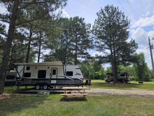 Travel Trailer on a gravel site with picnic table and fire pit at Leaning Pines Campground and Cabins