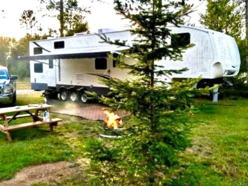 Parked trailer near fire pit and panic table at Plum Pines RV Park & Campground