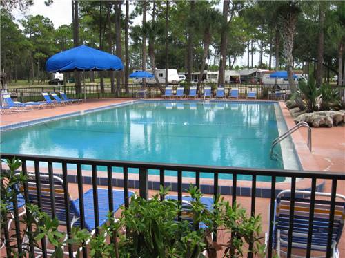 Rectangular swimming pool surrounded by iron fencing and lounge chairs, and large shade umbrella at ENCORE SUNSHINE HOLIDAY DAYTONA