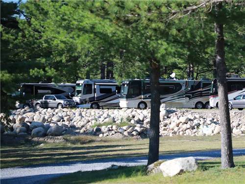 A row of Class A motorhomes parked along rocks at LAKE GEORGE RIVERVIEW CAMPGROUND