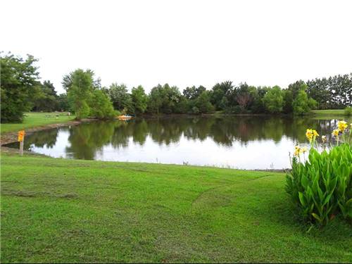 View of pond surrounded by grass, flowers and trees at FORT SMITH-ALMA RV PARK