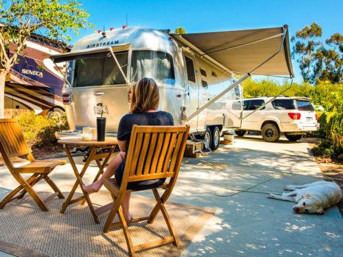 A lady sitting next to an Airstream trailer at ESCONDIDO RV RESORT